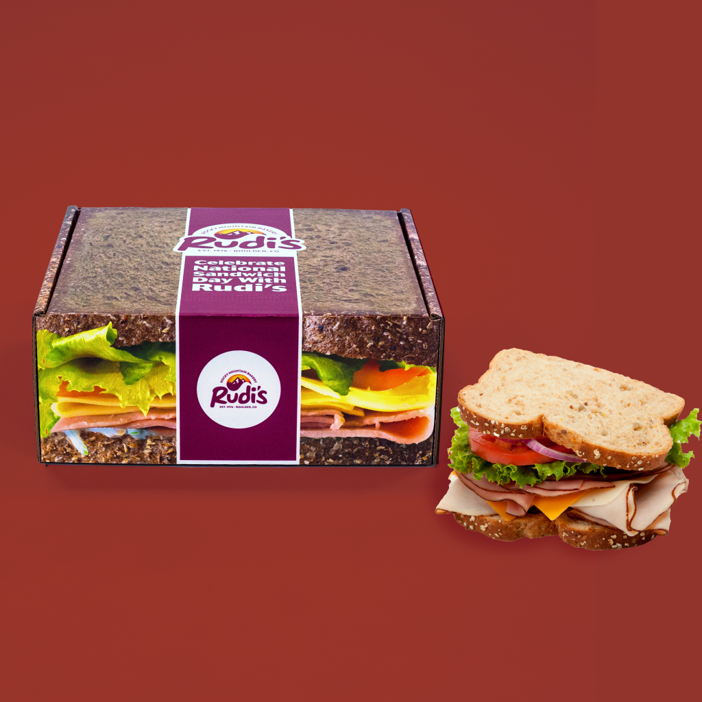mailer box with the image of a sandwich covering it, a "Rudi's" logo and a physical sandwich next to it